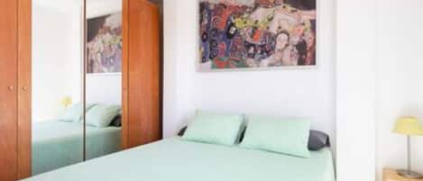 Un dormitorio con cama, un armario, un cuadro en la pared y una mesita de noche con lámpara.