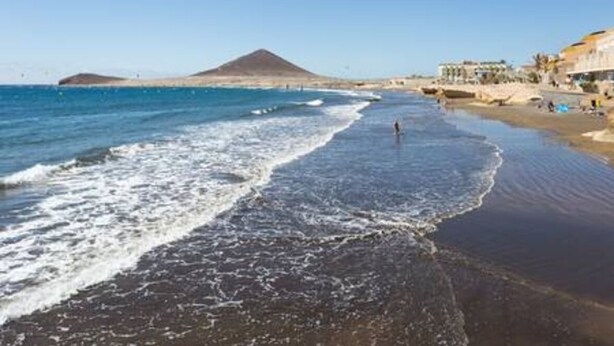 Une plage avec une montagne en arrière-plan, un rivage sablonneux et des bâtiments le long de la côte.