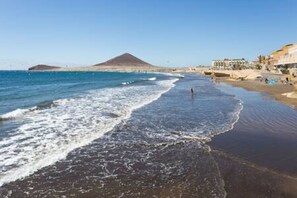 Une plage avec une montagne en arrière-plan, un rivage sablonneux et des bâtiments le long de la côte.