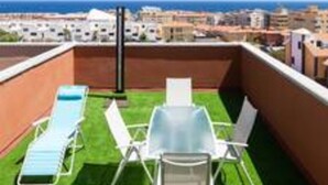 Une terrasse sur le toit, avec deux chaises longues et une table, offrant une vue sur le paysage urbain de la côte.