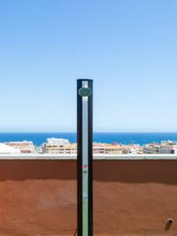 Un poteau vertical surmonté d’un objet circulaire, se dressant sur fond de ciel bleu dégagé et de paysage urbain côtier.