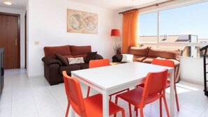 Un salon moderne avec une table à manger blanche et des chaises orange, un canapé marron avec des coussins et une grande fenêtre avec des rideaux.