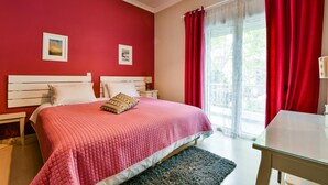 A bedroom with a bed, two bedside tables, a nightstand, a window with red curtains, and a view of greenery outside. - Star Acropolis apartment in Acropolis (Athens)