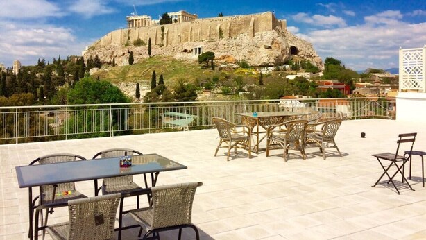 A terrace with wicker furniture and a table, overlooking a historic building on a hill. - Star Acropolis apartment in Acropolis (Athens)