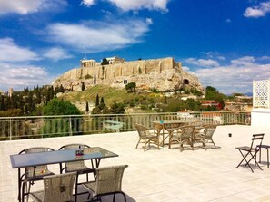 A terrace with wicker furniture and a table, overlooking a historic building on a hill. - Star Acropolis apartment in Acropolis (Athens)