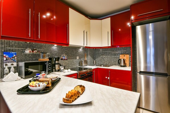 A modern kitchen with red cabinets, a stainless steel refrigerator, a microwave, and a coffee maker. - Star Acropolis apartment in Acropolis (Athens)
