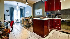 A modern kitchen with red cabinets, a central island, and a dining area with a chandelier. - Star Acropolis apartment in Acropolis (Athens)