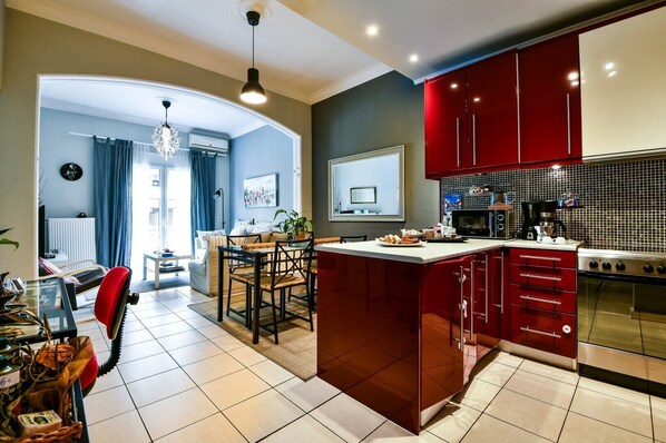 A modern kitchen with red cabinets, a central island, and a dining area with a chandelier. - Star Acropolis apartment in Acropolis (Athens)