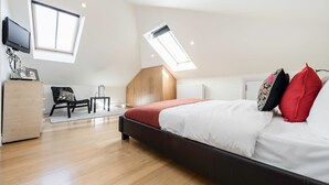 A modern bedroom with a large bed, skylights, a wooden floor, and a TV mounted on the wall. - Cosy 1 bedroom in Belsize Park (London)