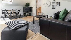 A modern living room with a black leather sofa, a black and white patterned ottoman, a small coffee table, and a dining area with a black and white striped rug. - Cosy 1 bedroom in Belsize Park (London)