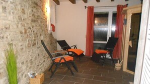 Une pièce chaleureuse aux murs de pierre, avec deux fauteuils noirs dotés de coussins orange, une petite table et une fenêtre ornée de rideaux rouges.