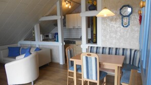 Un espace de vie compact comprenant un coin cuisine, un coin repas avec des meubles en bois et un canapé agrémenté de coussins bleus.