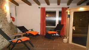 Une terrasse avec deux fauteuils et une table, un mur en pierre, une fenêtre avec des rideaux et une porte-fenêtre coulissante.