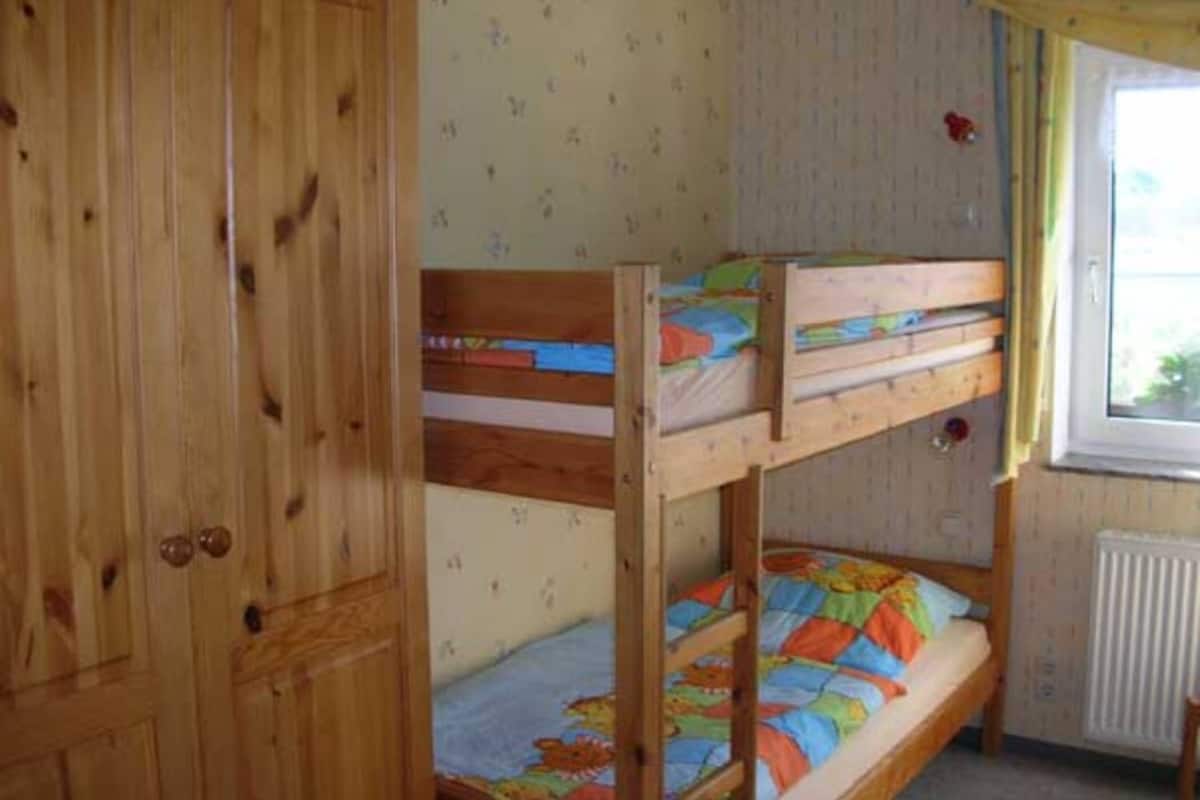 A bunk bed room with a wooden wardrobe and a window with curtains.