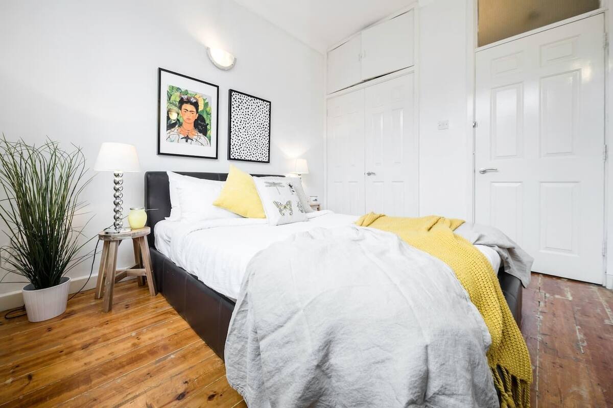 A bedroom with a bed, a bedside table with a lamp, a potted plant, and a wardrobe.
