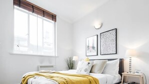 Et soveværelse med seng, natbord, lampe og et vindue.