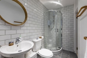 A modern bathroom with white subway tiles, a glass-enclosed shower, a white sink, and a toilet. - Old Compton Street Apartments (London)