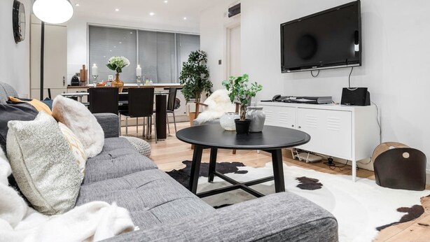 En moderne stue med en grå sofa, et rundt sofabord og et fjernsyn monteret på væggen.