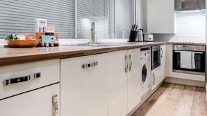 Et moderne køkken med træbordplade, indbyggede apparater og et stort vindue med rullegardiner.