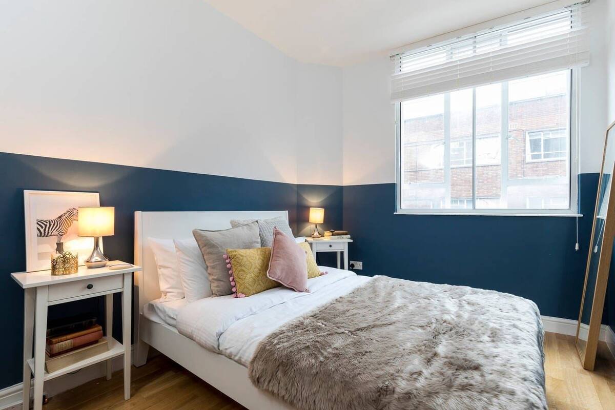 A bedroom with a bed, bedside tables, a window, and a view of buildings outside.
