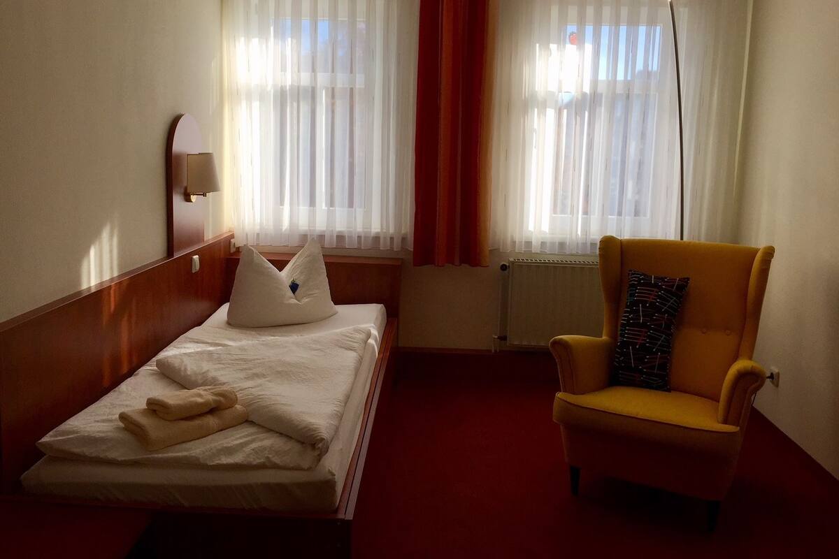 Ein Hotelzimmer mit Bett, einem Sessel, einer Heizung und einem Fenster mit Vorhängen.