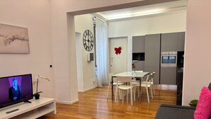 Un salon moderne doté d’un téléviseur à écran plat, d’un coin repas avec une table et des chaises, et d’une cuisine équipée d’appareils électroménagers.