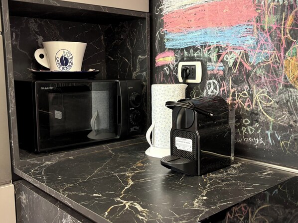 Una cocina con microondas, cafetera y pared decorada con una pizarra.