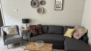 Ein Wohnzimmer mit grauem Sofa, einem Holztisch, einem grauen Sessel und einem gemusterten Teppich.
