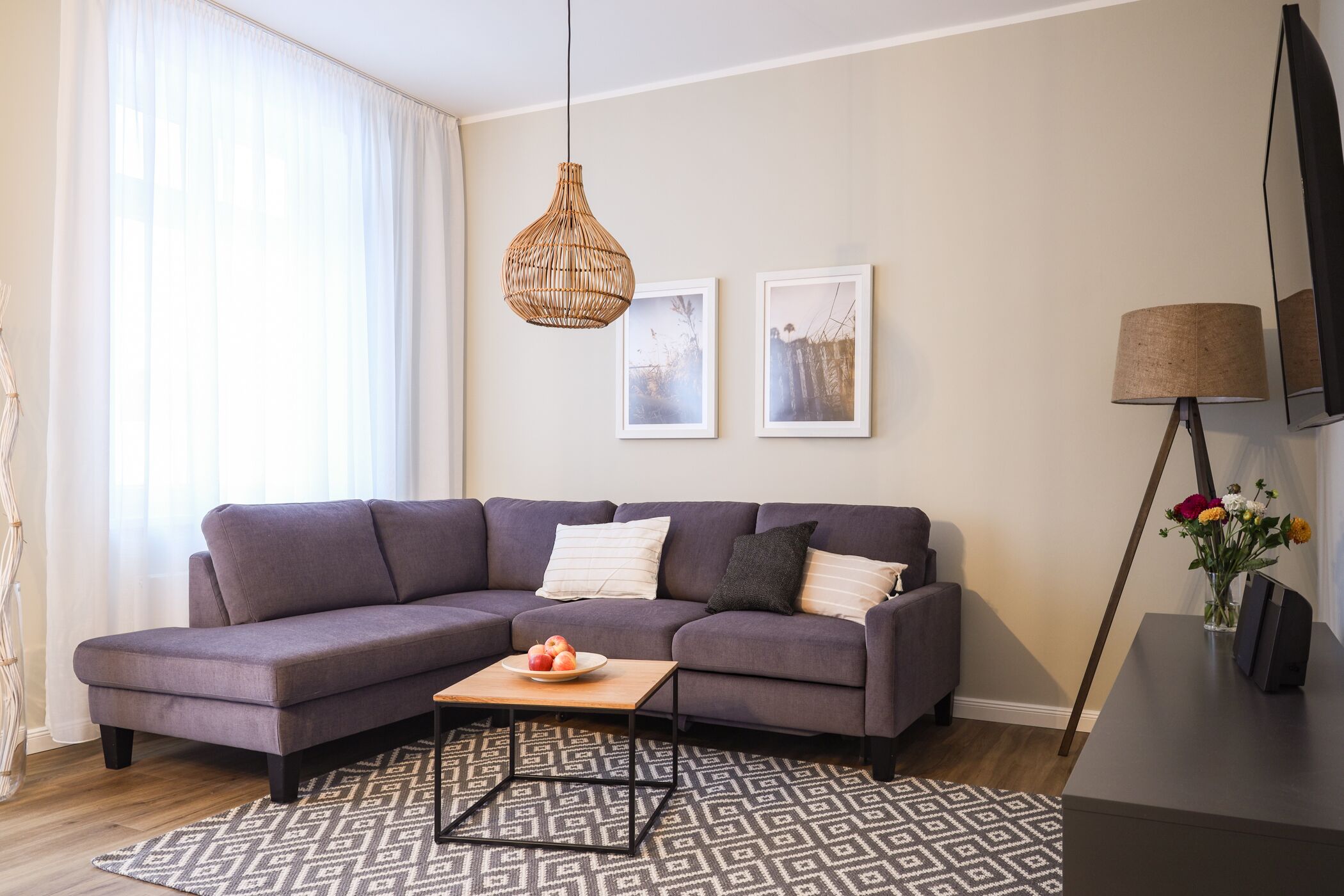 A modern living room with a sectional sofa, a coffee table, a patterned rug, a hanging light fixture, and framed artwork on the wall.