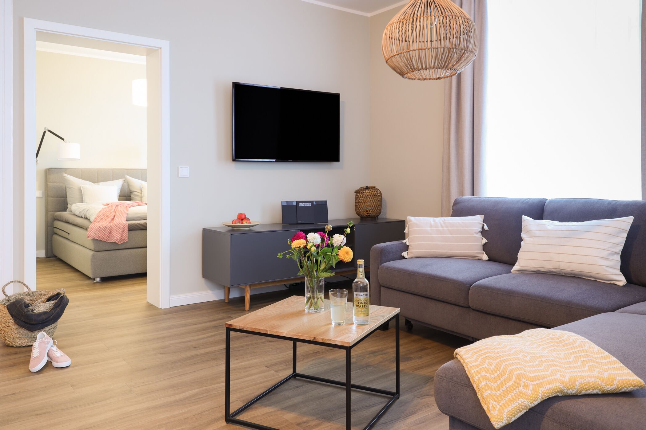 A modern living room with a sofa, a coffee table, a flat-screen TV, and a wicker pendant light.