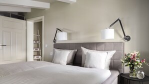 Un dormitorio ordenado con una cama grande, dos lámparas de noche, una mesita con un florero y un reloj.