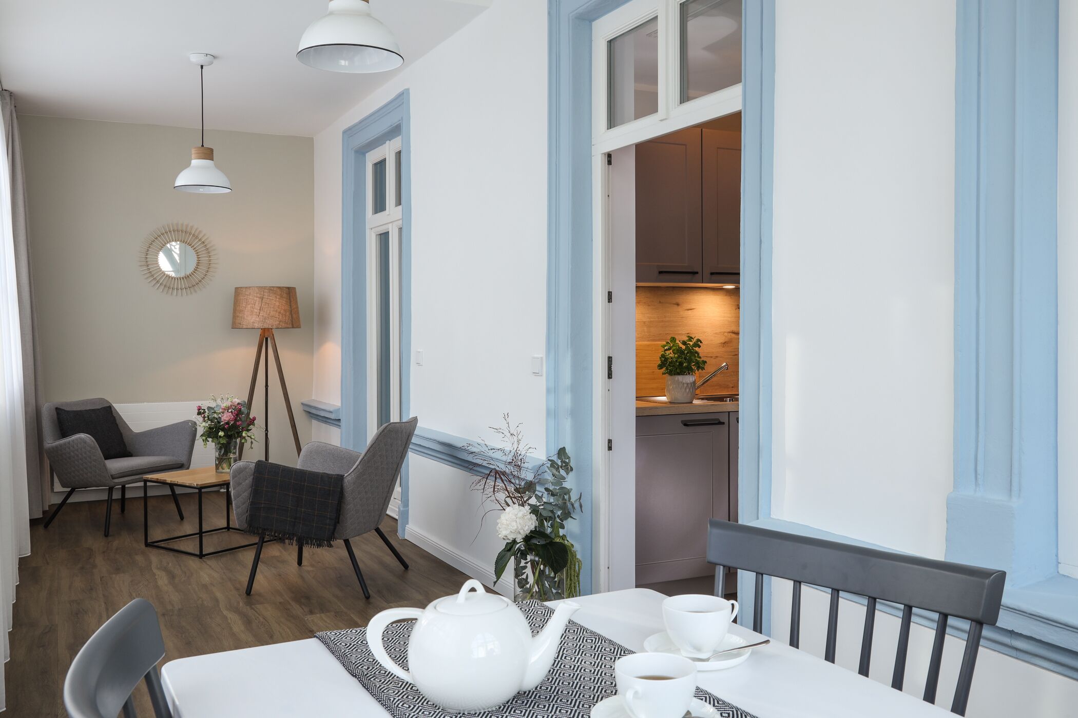 Hyggelig spiseplads med et bord dækket til to personer, en stol, en lampe og udsigt til køkkenet.