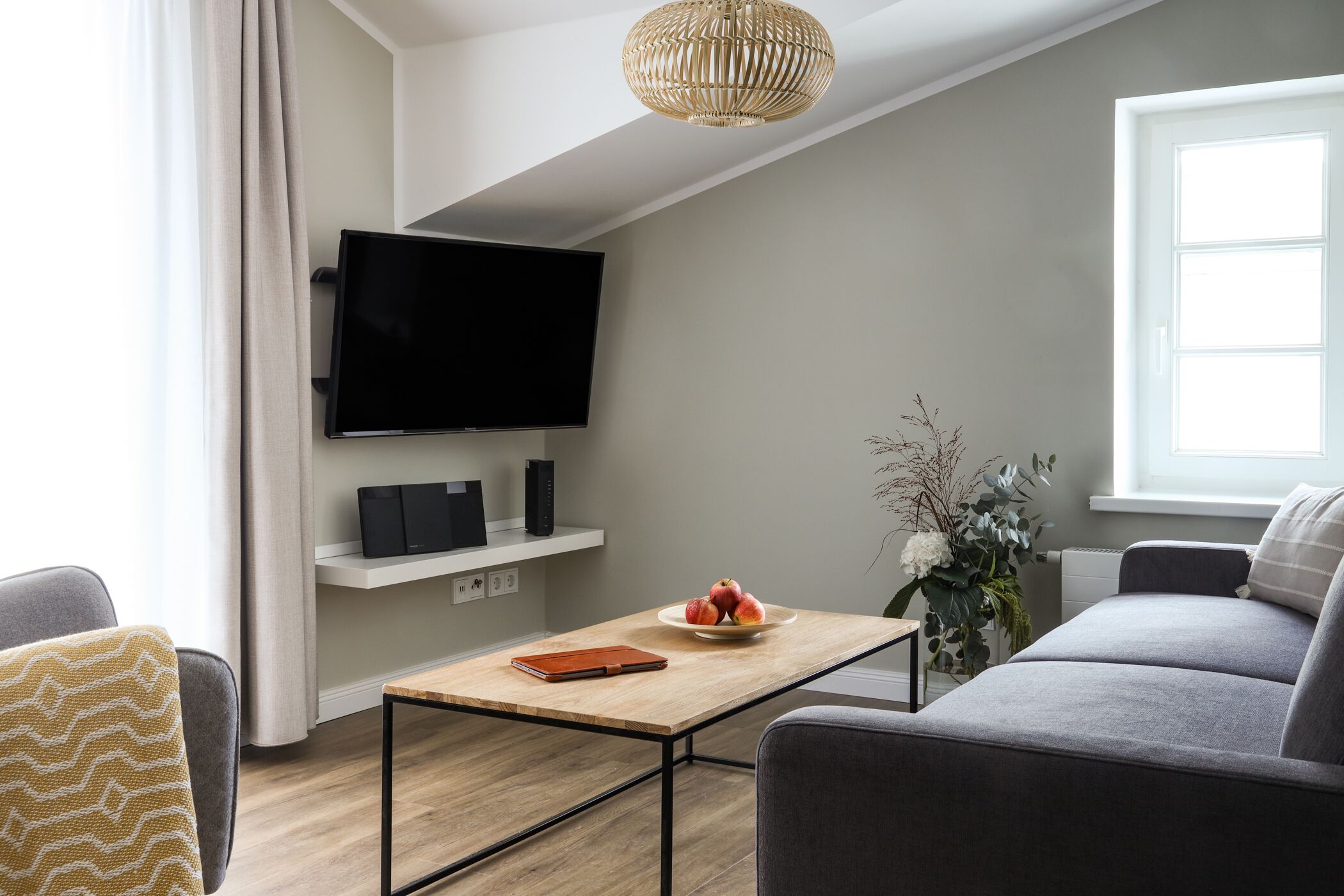 A modern living room with a flat-screen TV, a coffee table, a sofa, and a small table with a bowl of fruit.