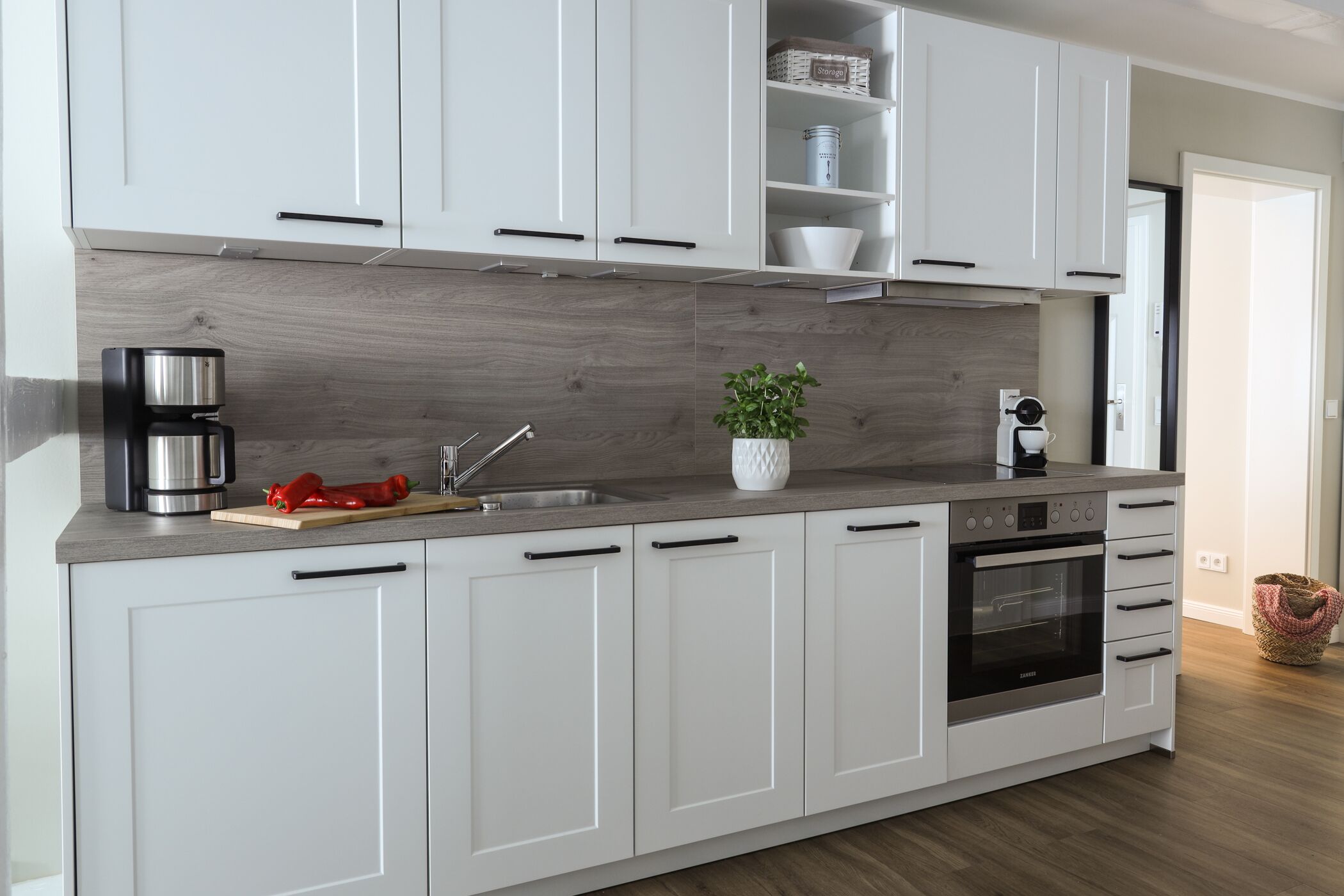 A modern kitchen with white cabinets, a stainless steel coffee maker, a red pepper, and a potted plant.