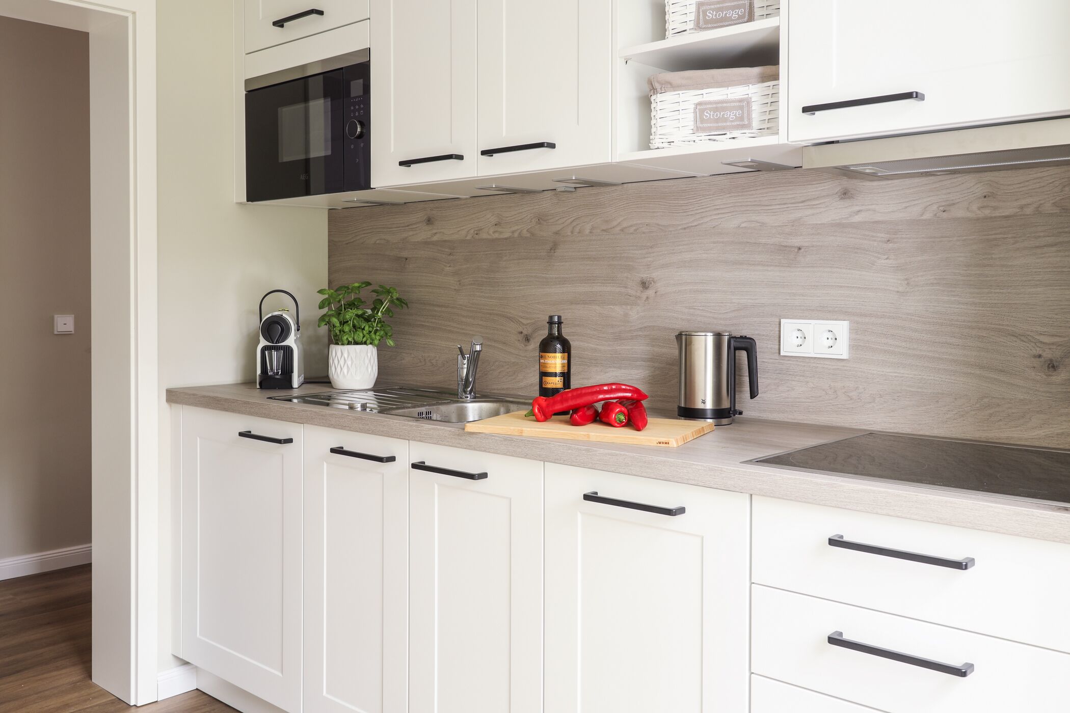 A modern kitchen with white cabinets, a wooden backsplash, a built-in microwave, and a coffee maker on the countertop.