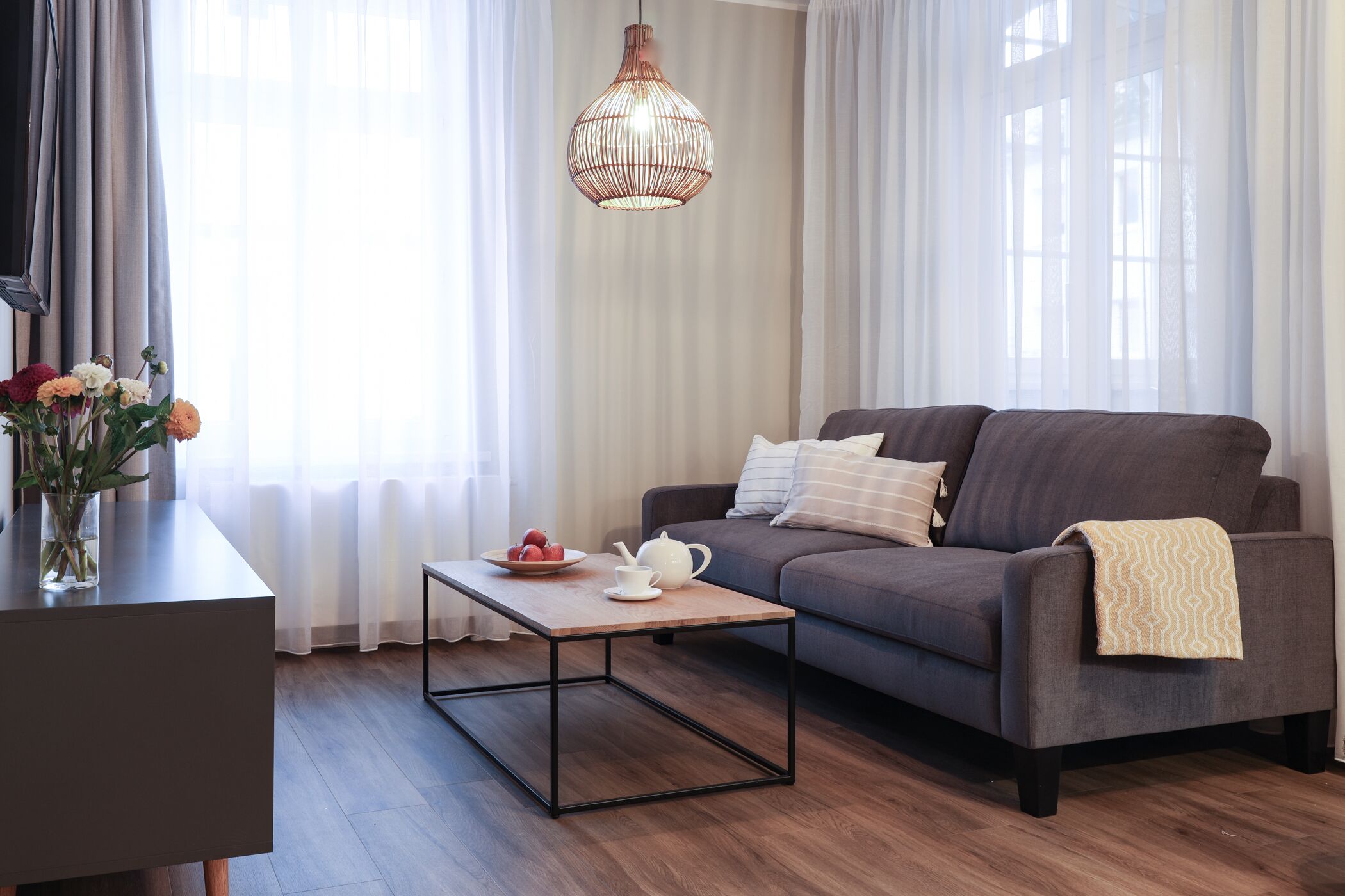 A modern living room with a grey sofa, a wooden coffee table, a vase with flowers, and a hanging light fixture.