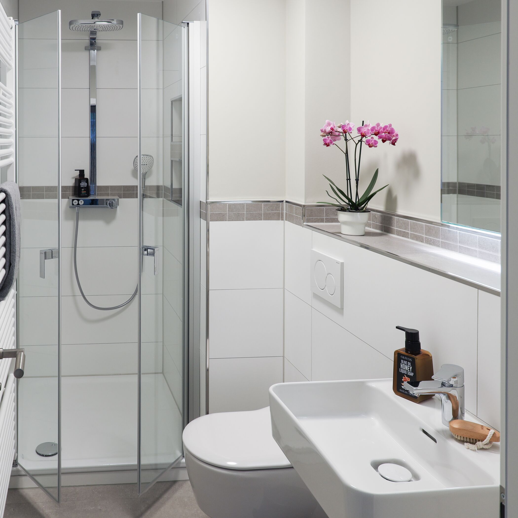 Un baño moderno con ducha envuelta en vidrio, inodoro blanco y lavamanos con dispensador de jabón.