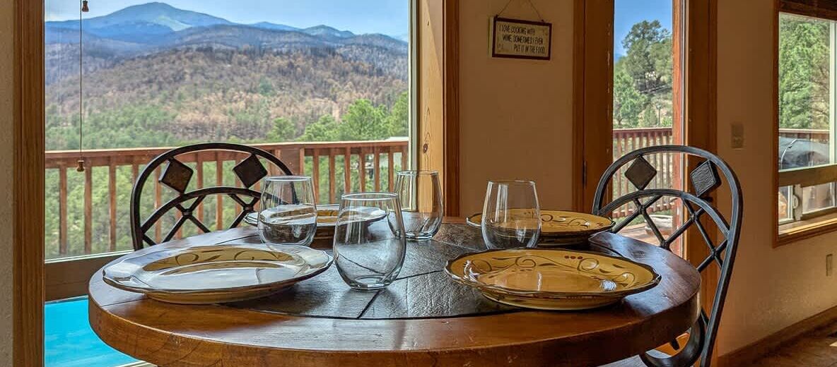 Una mesa de comedor con platos y vasos, con vistas a una montaña pintoresca.