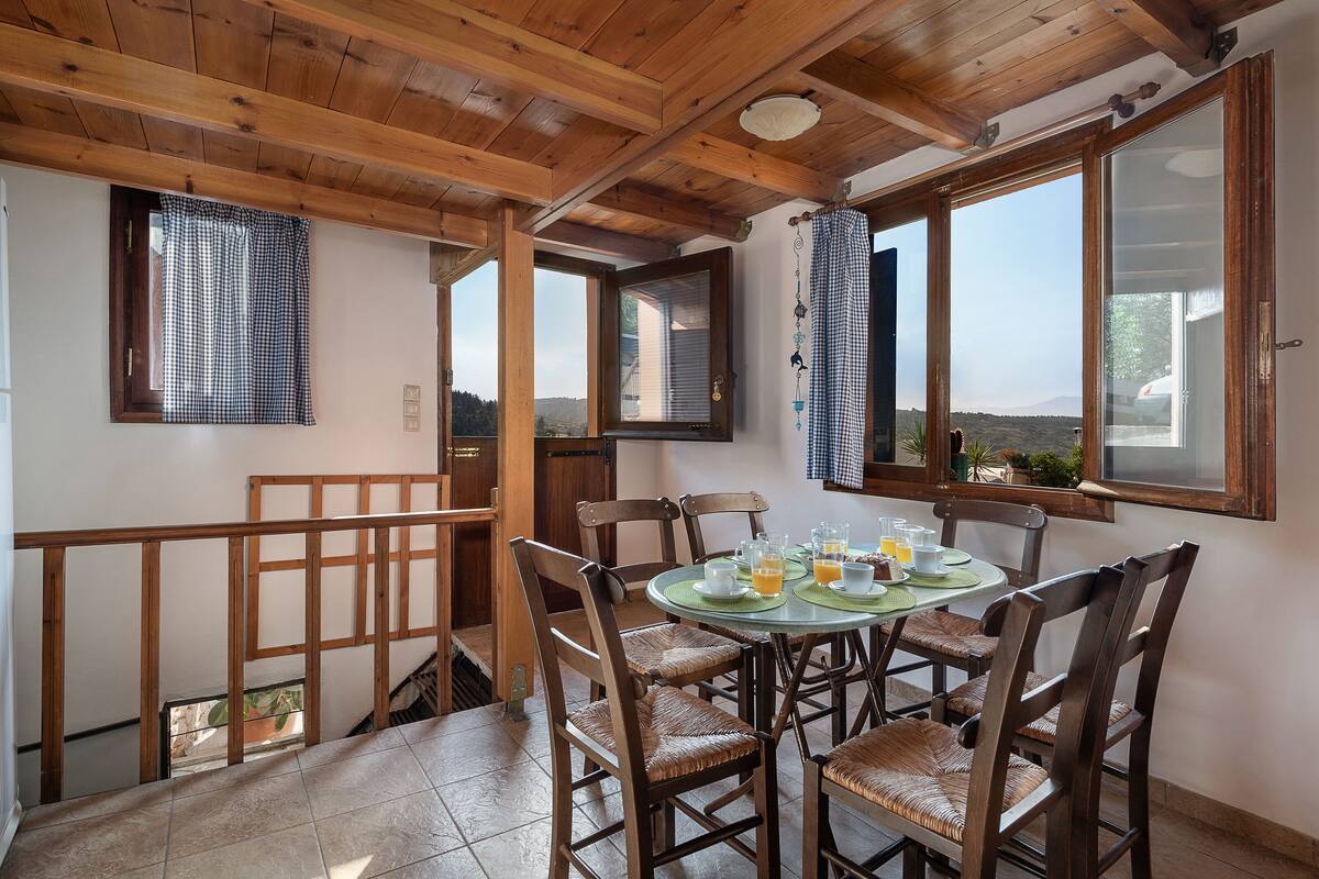 A dining area with a wooden ceiling, checkered curtains, and a table set for four with glasses of orange juice.