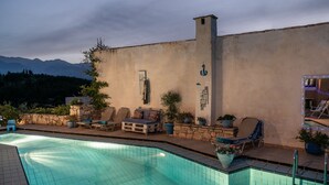 A swimming pool with lounge chairs and potted plants, set against a backdrop of mountains and a cloudy sky. - Kritiko Arhontiko (Apokoronas)