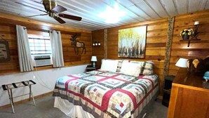 A bedroom with a bed, a ceiling fan, a window with curtains, a wall-mounted lamp, and a painting. - River Cabin (Ruidoso)