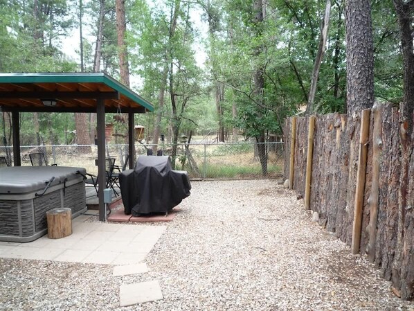 Un espace extérieur aménagé, abrité et doté d’un barbecue, d’un jacuzzi et d’une clôture en bois.
