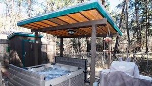 A hot tub under a wooden pergola with a small shed in the background. - River Cabin (Ruidoso)