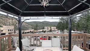 Eine Terrasse im Freien mit Tisch und Stühlen, einer schwarzen Markise und Blick auf eine Stadt mit Gebäuden und Hügeln im Hintergrund.