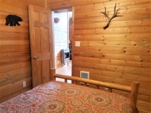 Quarto de cabana de madeira com uma cama, porta, chifres fixados na parede e decoração com urso.