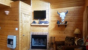 Ein Holzblockbau-Innenraum mit Kamin, einem angebrachten Fernseher und einem aufgehängten Kuhschädel.