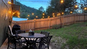 Une terrasse extérieure avec une table ronde et des chaises, des guirlandes lumineuses et une clôture en bois.