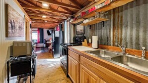 Une cuisine avec des meubles de rangement en bois, un évier et une cuisinière. Le plafond est en bois, avec des poutres apparentes.
