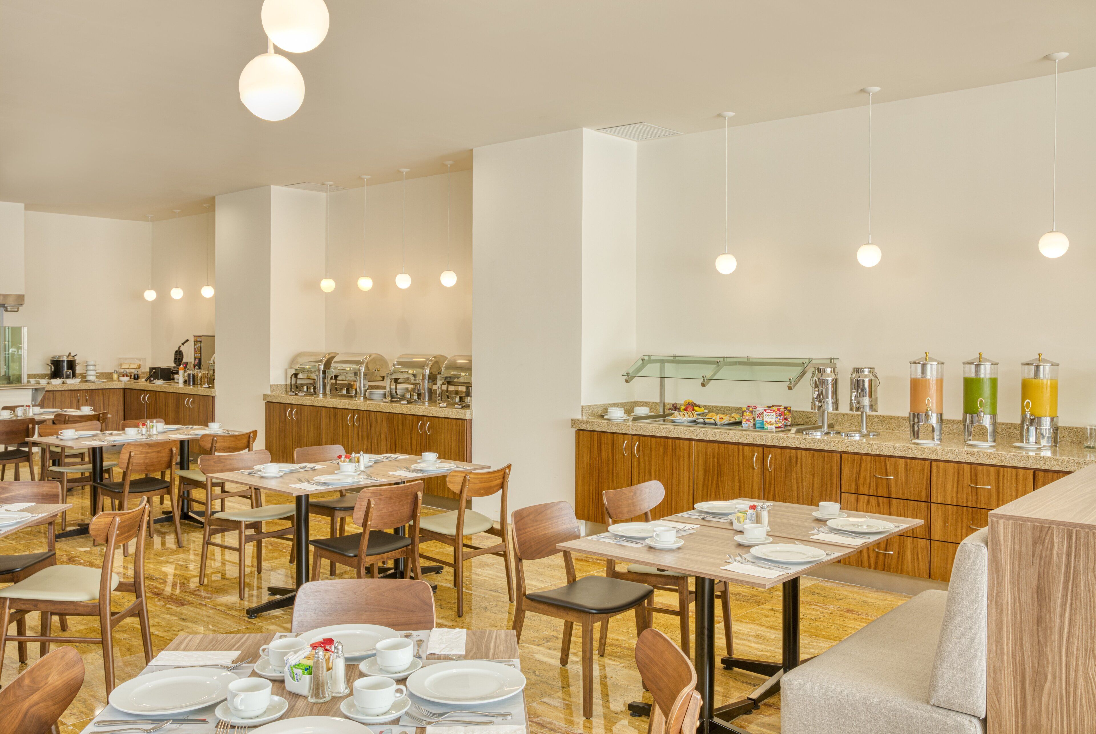Een ruime eetruimte met meerdere tafels en stoelen, een buffet en hangende lampen.