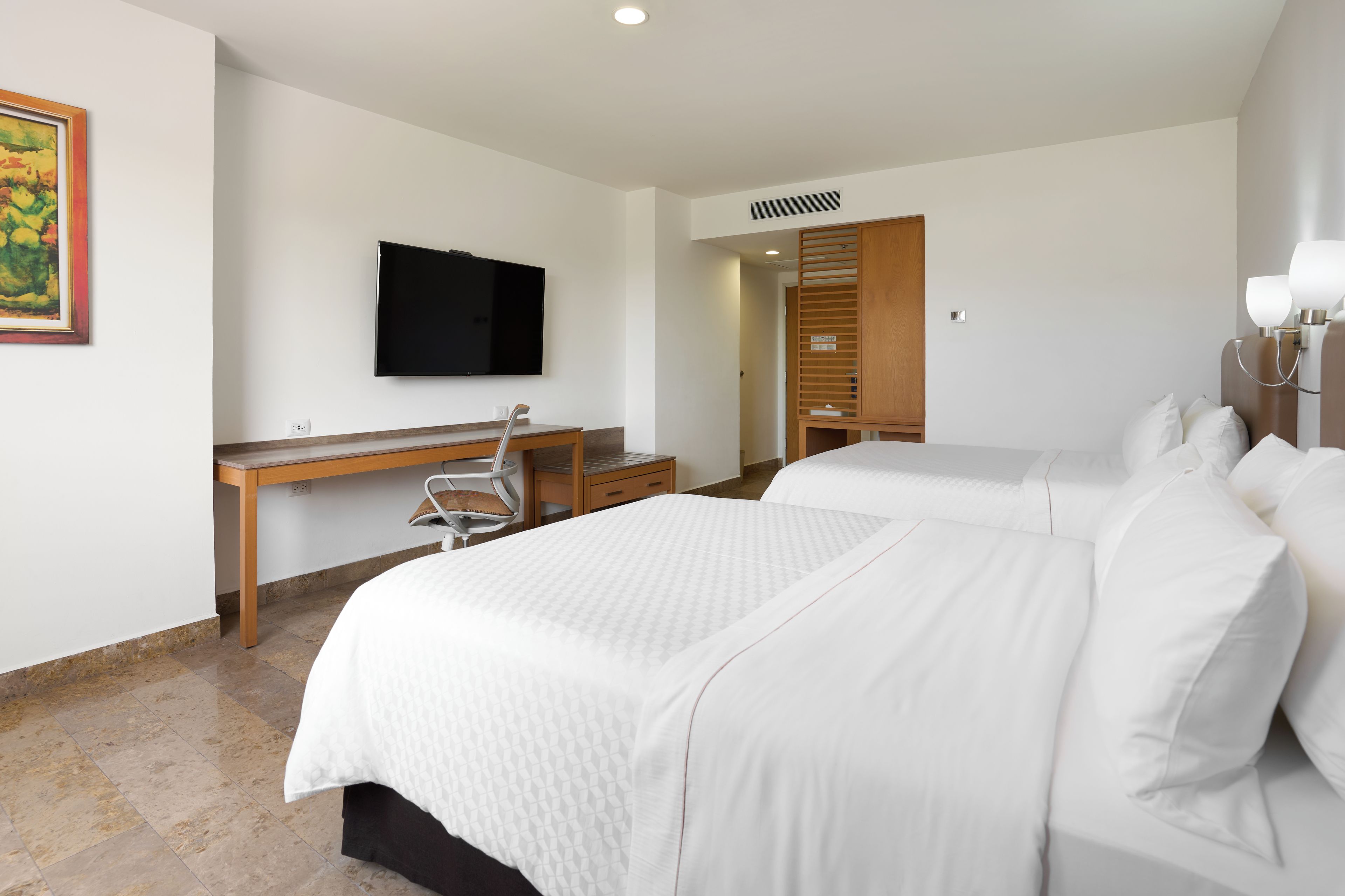 Una habitación de hotel con una cama, un escritorio, una silla, un televisor y un armario.